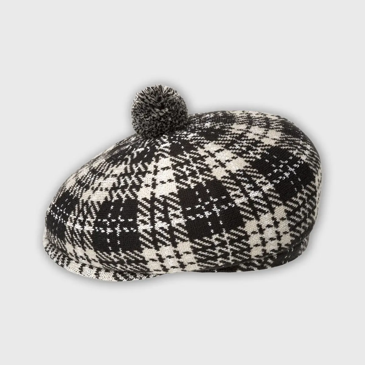 Zijaanzicht van Kangol cap met pom-pom, tonend grof gebreid zwart-wit textiel en klassieke flat cap vorm.