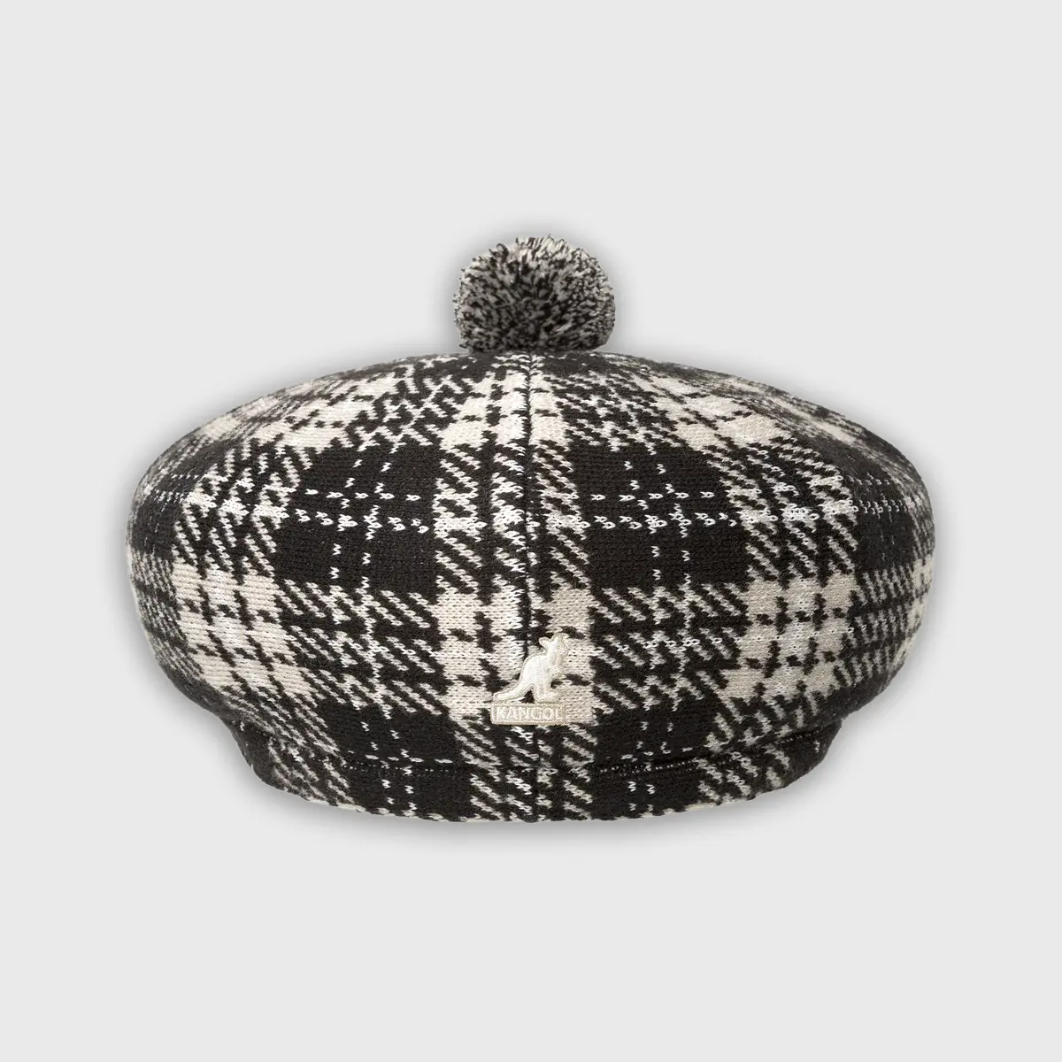 Kangol gebreide baret in zwart-wit ruitpatroon, detailopname van achterkant met geborduurd zilveren kangoeroe-logo en pom-pom.