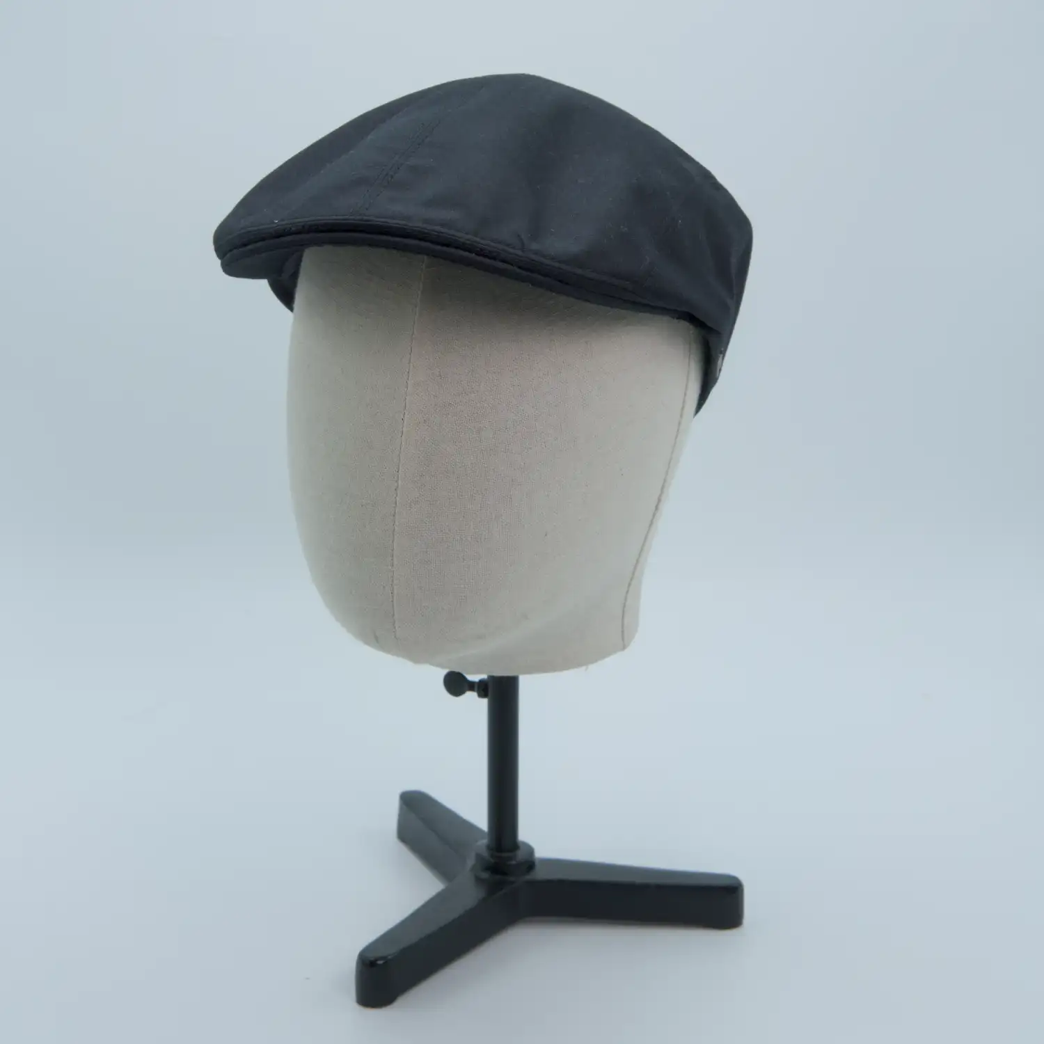 Casquette plate étroite en coton noir. Posée sur une tête de mannequin.