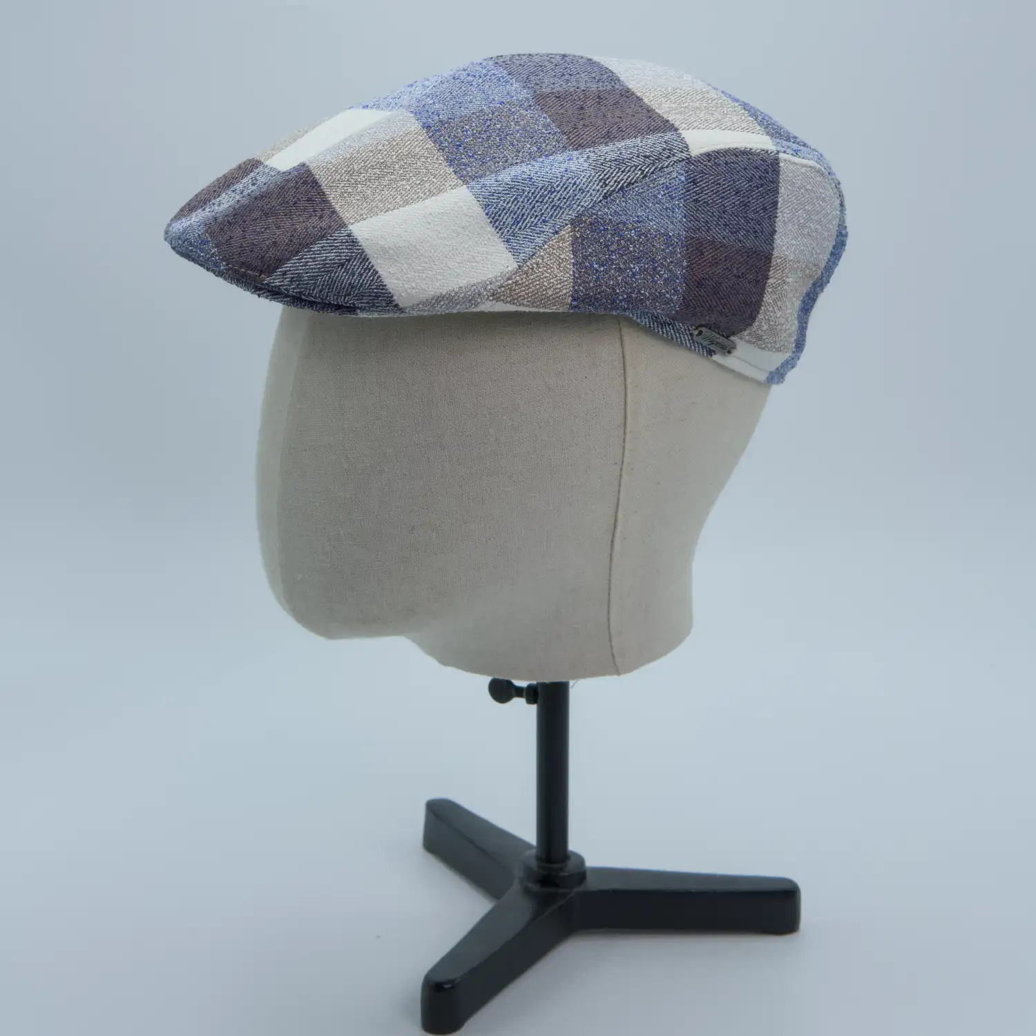 Casquette plate en mélange lin et laine multicolore à carrés gris, bleus et bruns, présentée sur une tête de mannequin.