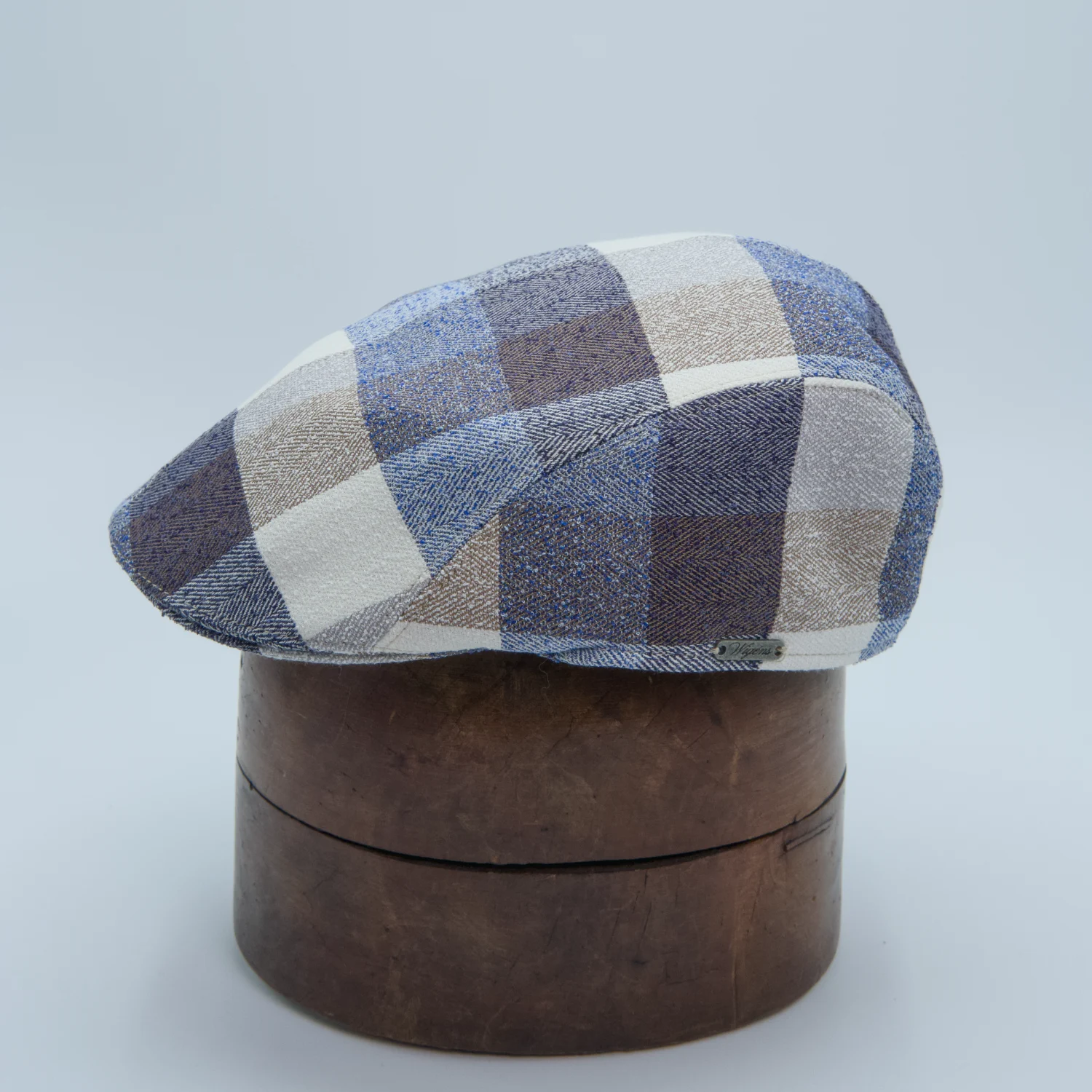 Casquette plate en mélange lin et laine multicolore à carrés gris, bleus et bruns, présentée sur une tête de présentation.