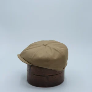 Casquette newspaper boy camel, brun clair, en matière imperméable, posée sur une forme à chapeau.