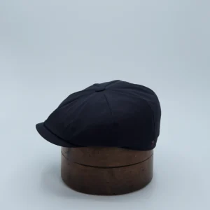 Casquette newspaper boy noire, en matière imperméable, posée sur une forme à chapeau.